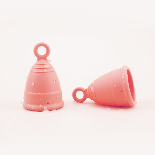 Two peach menstrual cups, one standing, one on its side, both with right for easy extraction